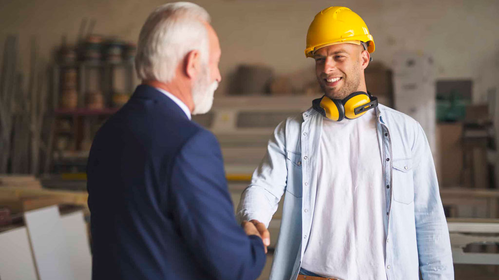 Artisan et client discutant d'un projet devant des plans dans un atelier bois